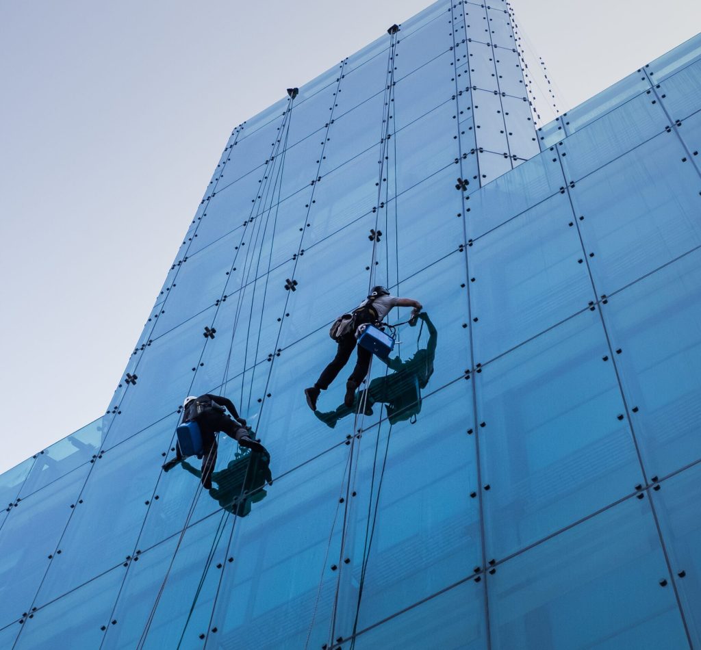 A vertical low angle shot of two people climbing a tall glass building during the day time